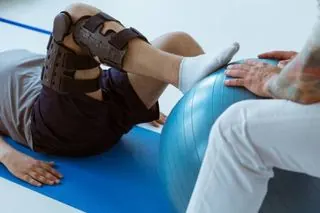 Patient sitting on a gym mat training with an exercise ball during post-operative rehabilitation at home